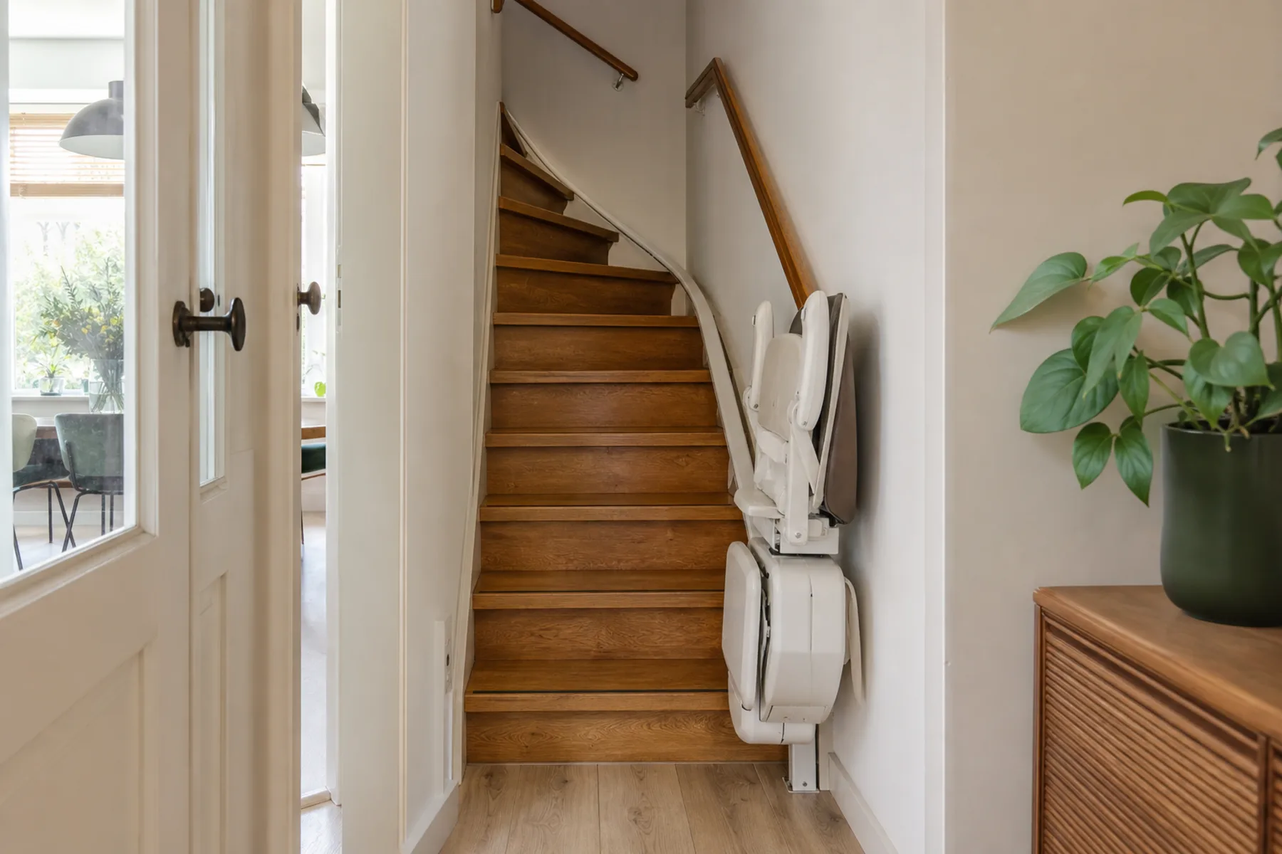Compacte traplift, opgeklapt langs een houten trap in een licht Nederlands huis (sfeerbeeld)